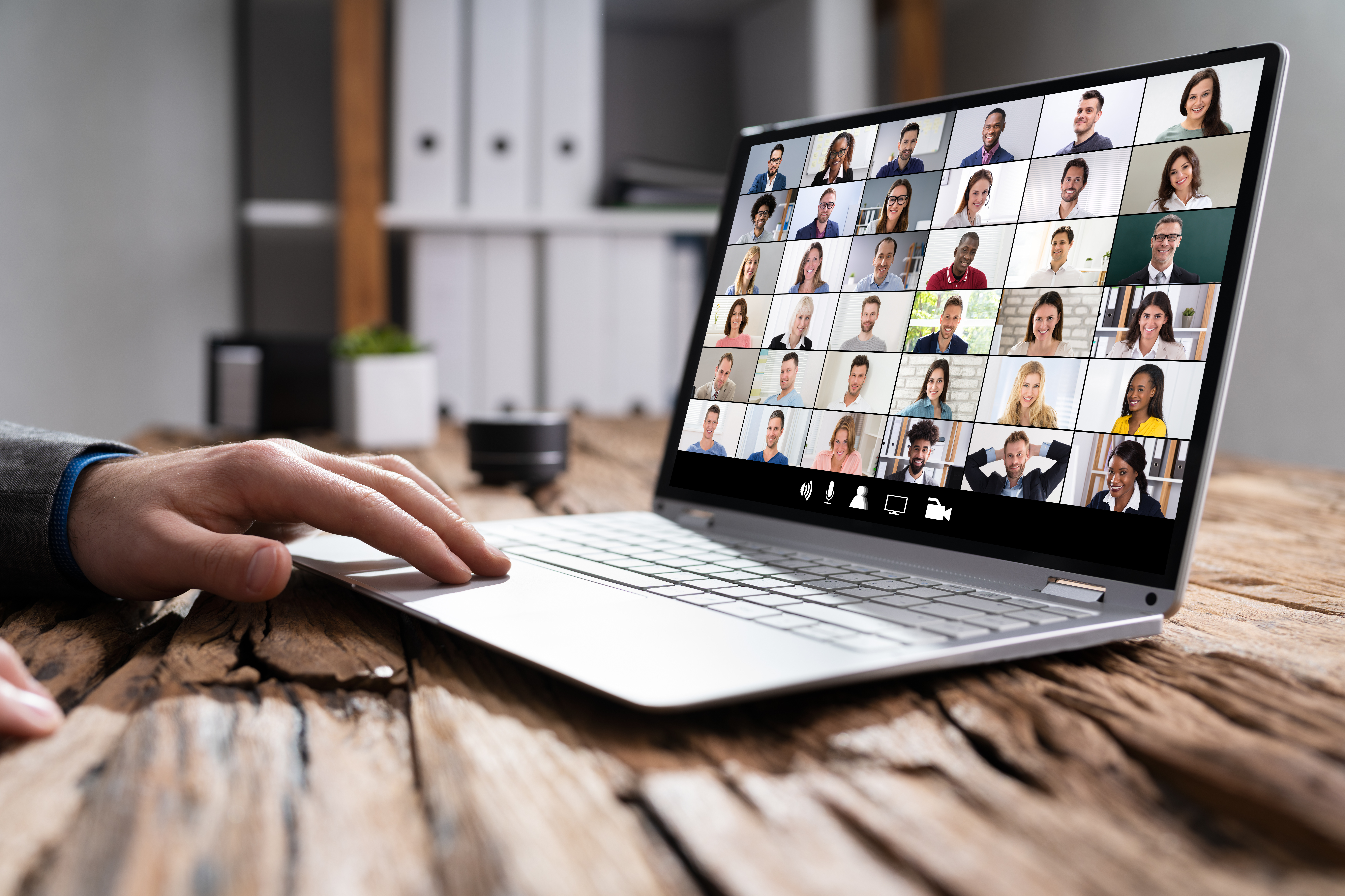 photo of an open laptop with a hand on the keyboard and a variety of faces in the Zoom windows on the screen